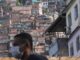 Man wearing a white mask with a favela as background. Photo by: Ricardo Moraes/Reuters