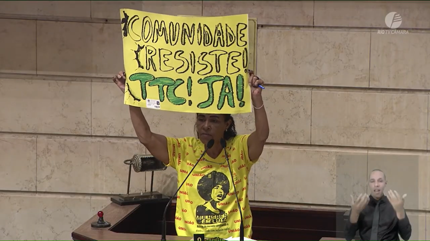 Jurema Constâncio, of the Shangri-Lá Housing Cooperative and the National Union for Popular Housing (UNMP) holds a sign reading “Communities Resist! CLT Now!” during her speech at the public hearing on the Master Plan. Source: Chamber TV.