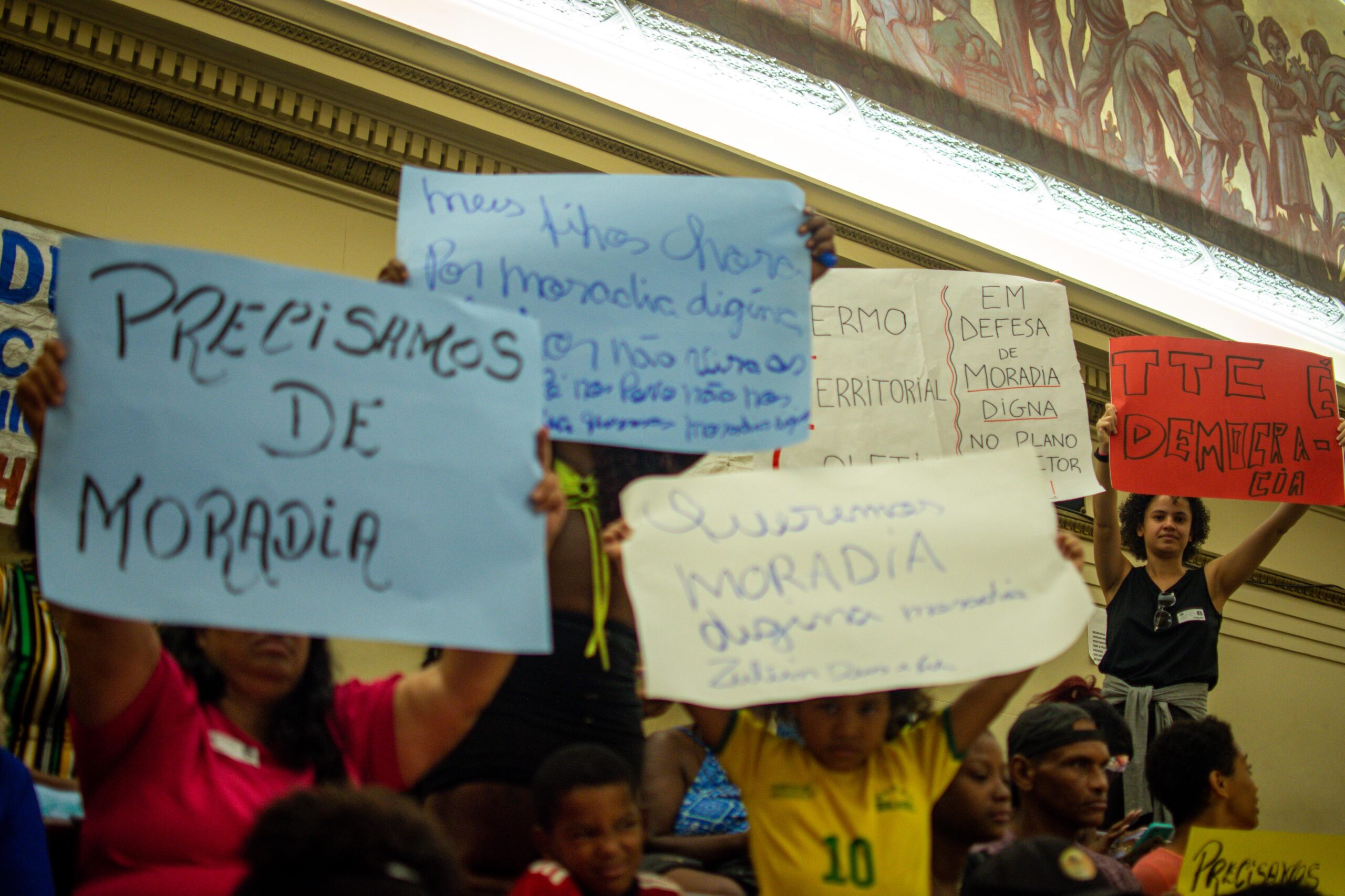 People at the Master Plan Public Hearing at Rio City Council Chambers on April 5, 2023 holding signs calling for decent housing and supporting the Favela Community Land Trust (F-CLT)