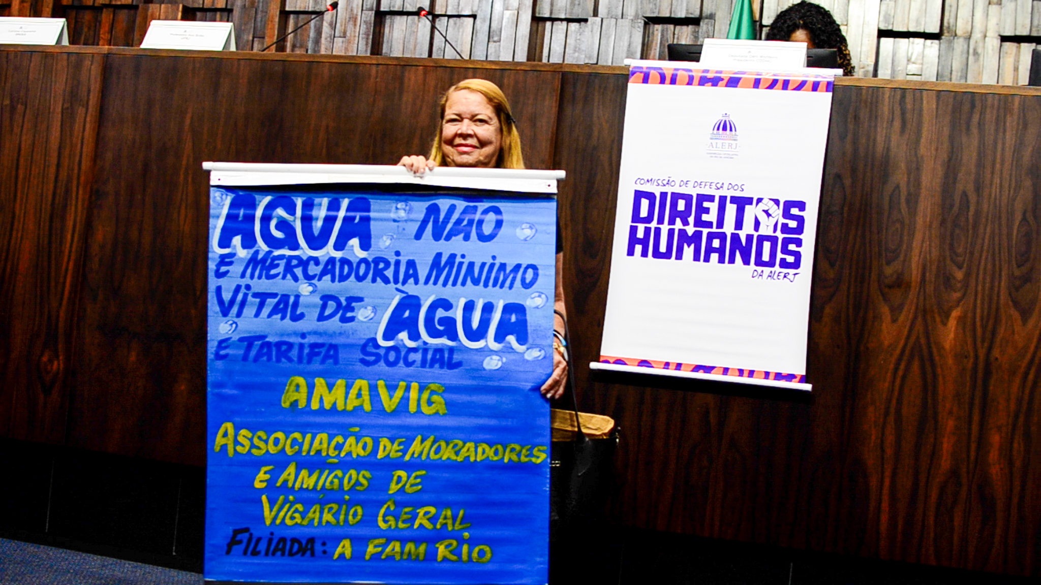 Citizen holds a sign that reads ‘Water is not a commodity! Vital minimum water and social tariff! Amavig – Association of Residents and Friends of Vigário Geral’. Photo: Patricia Schneidewind