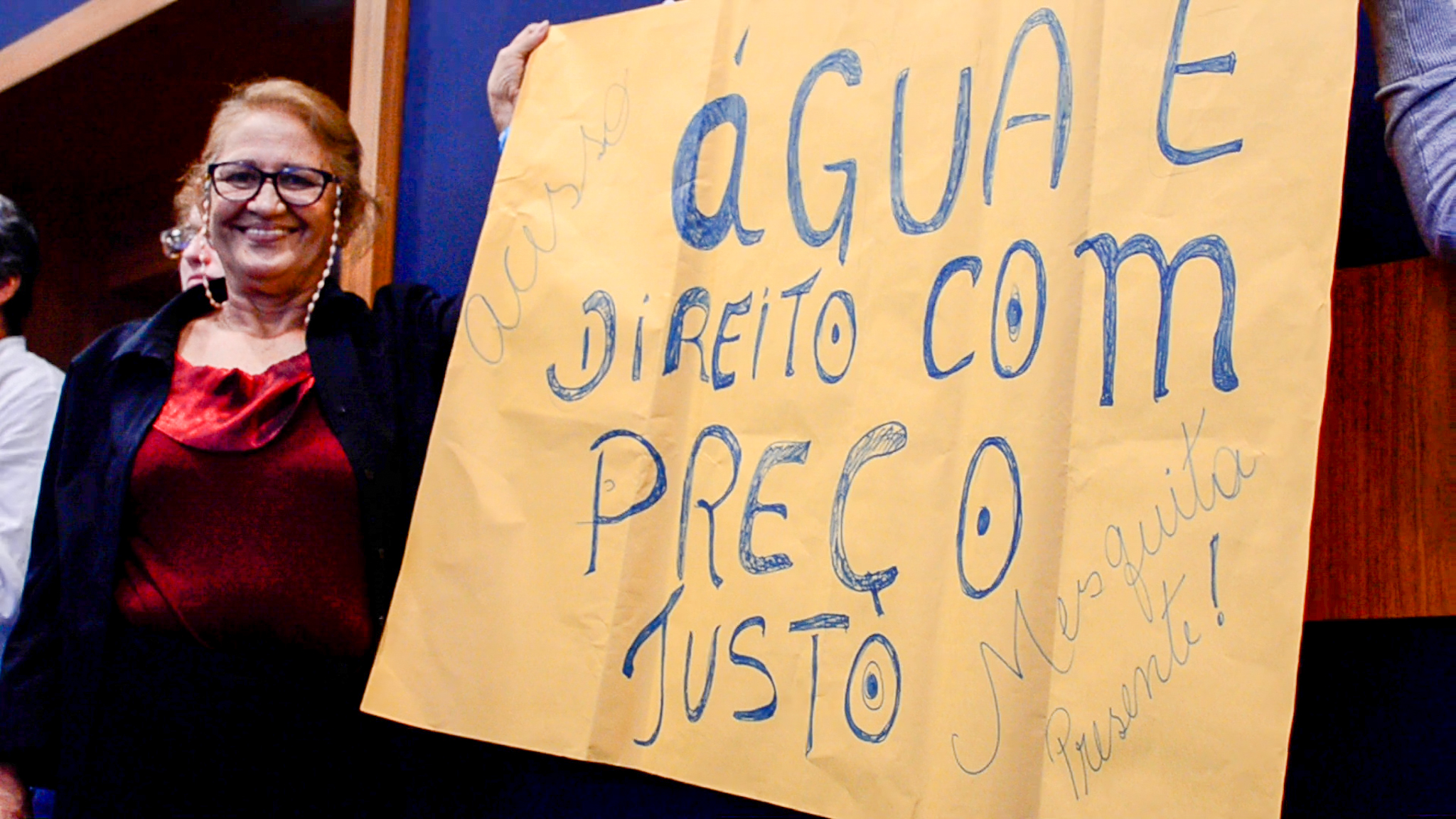 Mesquita resident at the Public Hearing with a poster that reads "Water is a right! At a fair price!" Photo: Patricia Schneidewind
