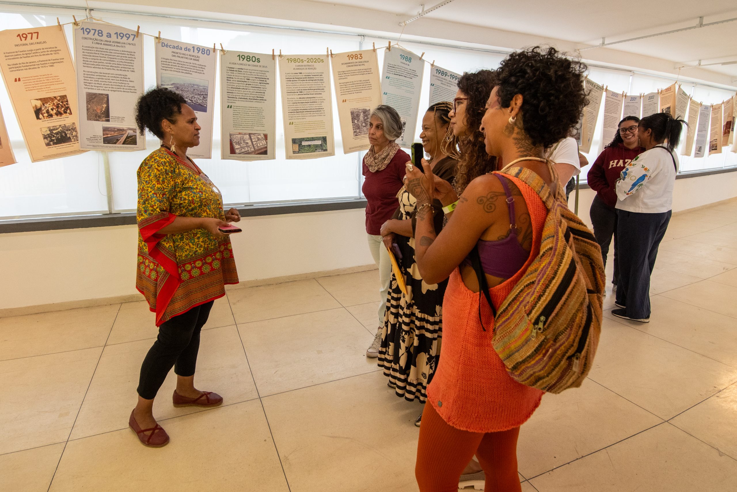 Márcia Souza (left) guides visitors through the ‘Favela Climate Memory’ exhibition, where they can explore the timeline panels, the Basin of Memories and a wealth of content on the climate memories of ten Rio de Janeiro favelas. Photo: Bárbara Dias Márcia Souza (left) guides visitors through the ‘Favela Climate Memory’ exhibition, where they can explore the timeline panels, the Basin of Memories and a wealth of content on the climate memories of ten Rio de Janeiro favelas. Photo: Bárbara Dias