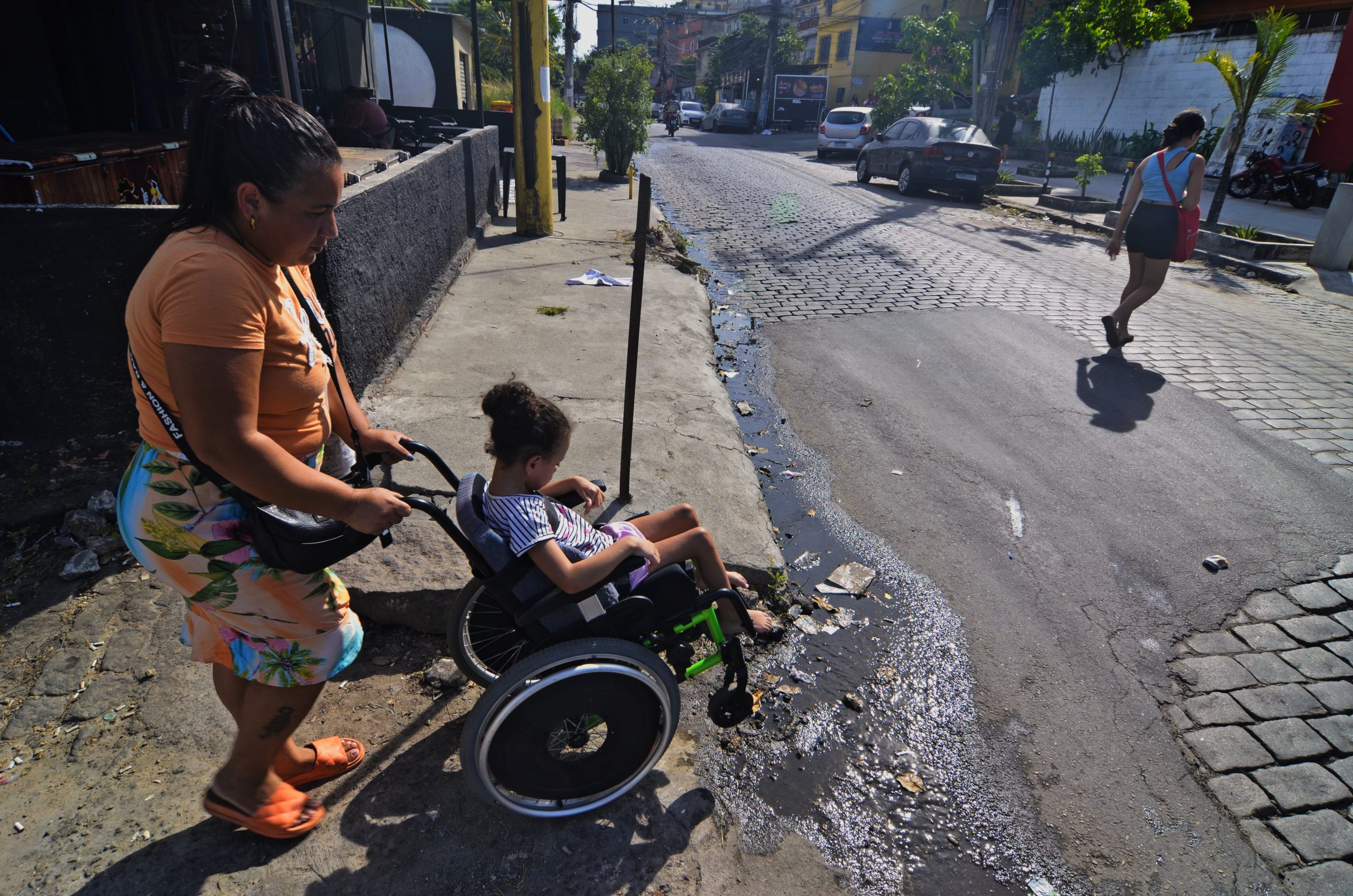 Forced to push her daughter's wheelchair through open sewage, Ana Raquel de Almeida Rocha, 37, climbs Morro do Timbau with Eloá de Almeida Villela Ezedim to reach their home. Photo: Ramon Vellasco Forced to push her daughter's wheelchair through open sewage, Ana Raquel de Almeida Rocha, 37, climbs Morro do Timbau with Eloá de Almeida Villela Ezedim to reach their home. Photo: Ramon Vellasco